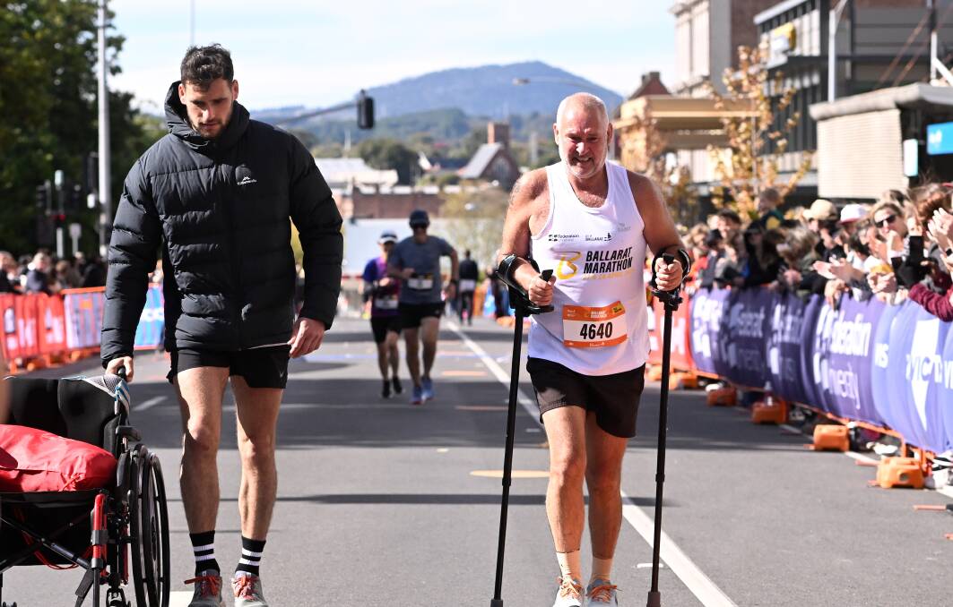 Ballarat's Mick Marshall crosses the line after walking the half marathon on crutches with his support team member Aiden Domic (left). Picture by Adam Trafford